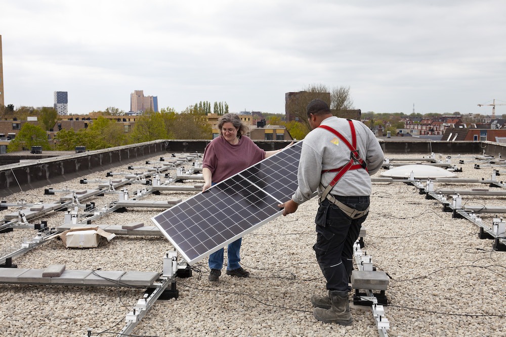 Musetta Blaauw (initiatiefnemer coöperatie GOED) legt samen met de installateur de eerste zonnepaneel op het dak van Lentis aan de Hereweg neer.