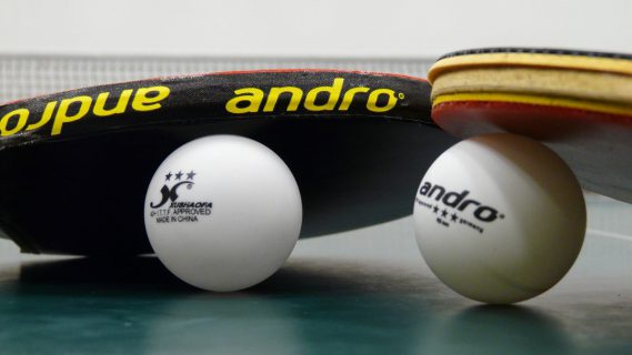 Sfeerafbeelding van twee tafeltennisbatjes op een tafeltennistafel en twee tafeltennisballetjes.