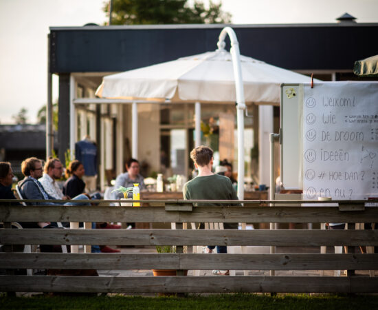 Overleg van jongeren die buiten praten over de invulling van De Bazenfabriek. Op de voorgrond staat en bord waarop de punten staan die ze gaan bespreken.