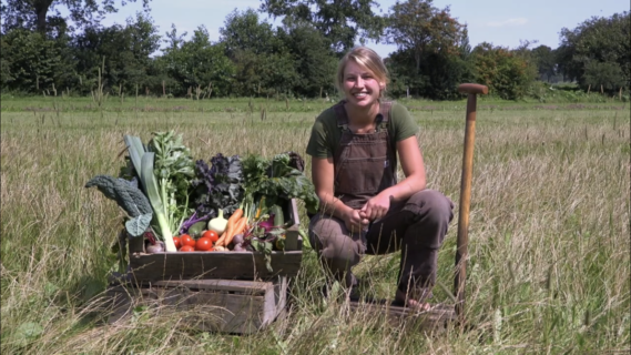 De drijfveer achter Tuinderij Het Groeipunt, Esther Kuiper, zit gehurkt naast een kratje met groenten.