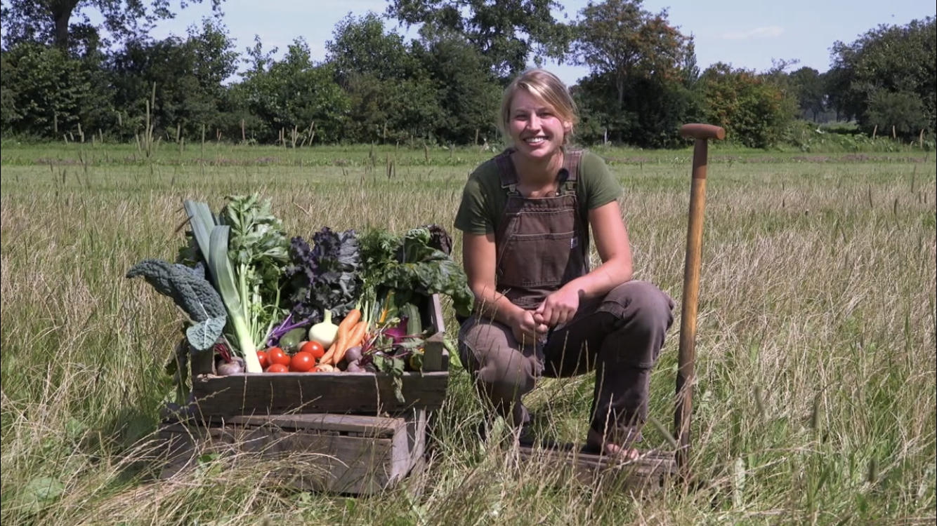 De drijfveer achter Tuinderij Het Groeipunt, Esther Kuiper, zit gehurkt naast een kratje met groenten.