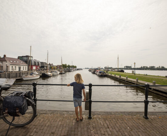 Decoratieve afbeelding van kind die op een brug in Zoutkamp over het water uitkijkt.