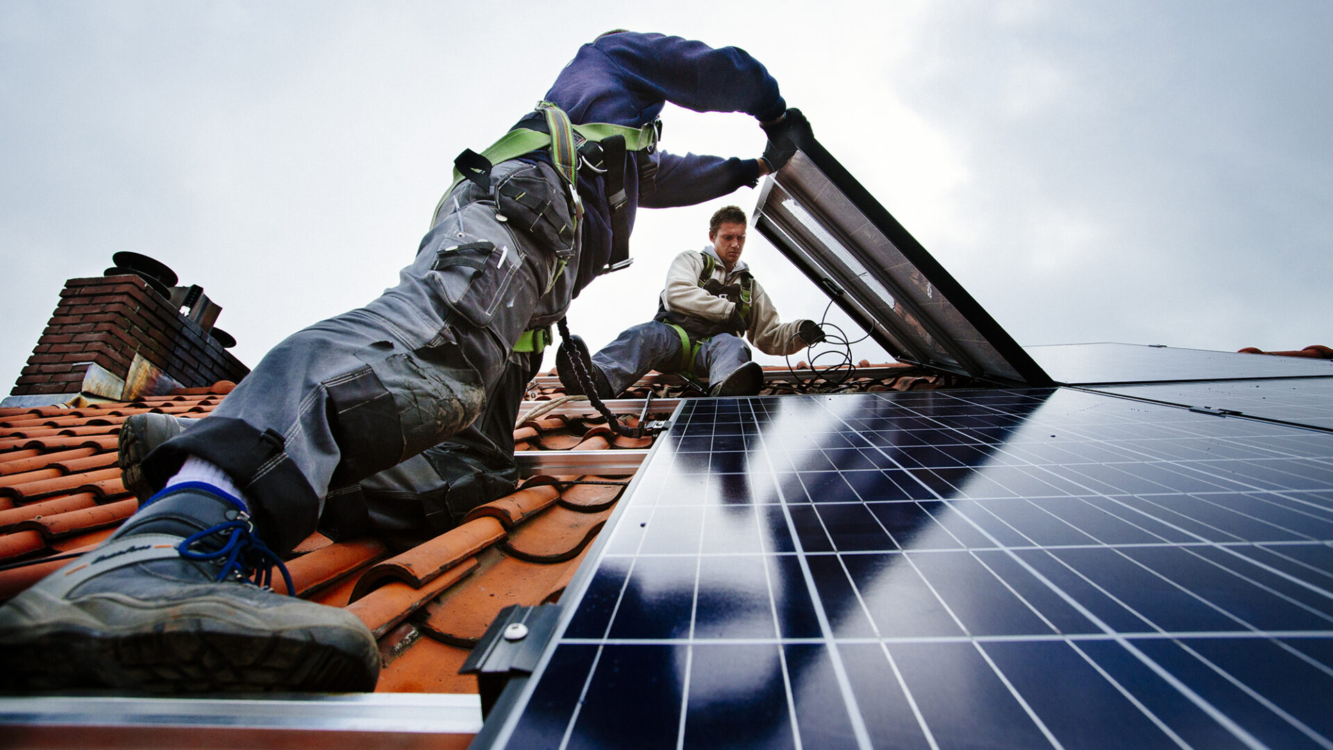 Decoratieve afbeelding van twee mannen bezig zijn met zonnepanelen op een dak te leggen.