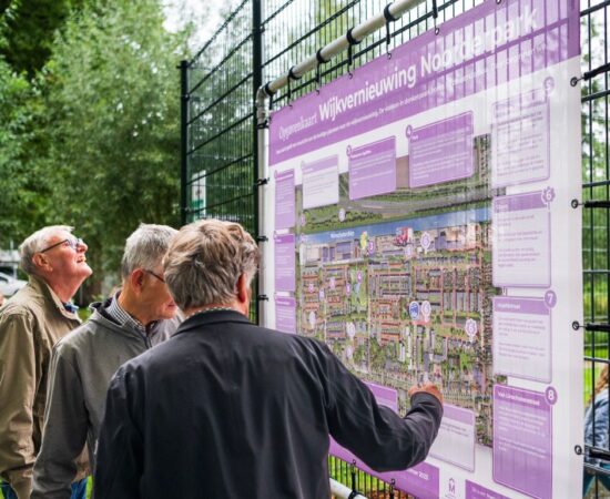 Buurtbewoners kijken naar een bord met de vernieuwingsplannen voor Hoogezand-Noord