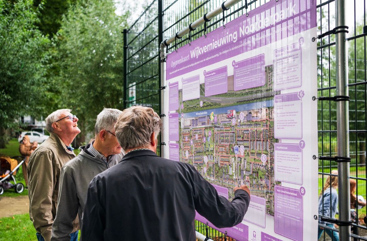 Buurtbewoners kijken naar een bord met de vernieuwingsplannen voor Hoogezand-Noord
