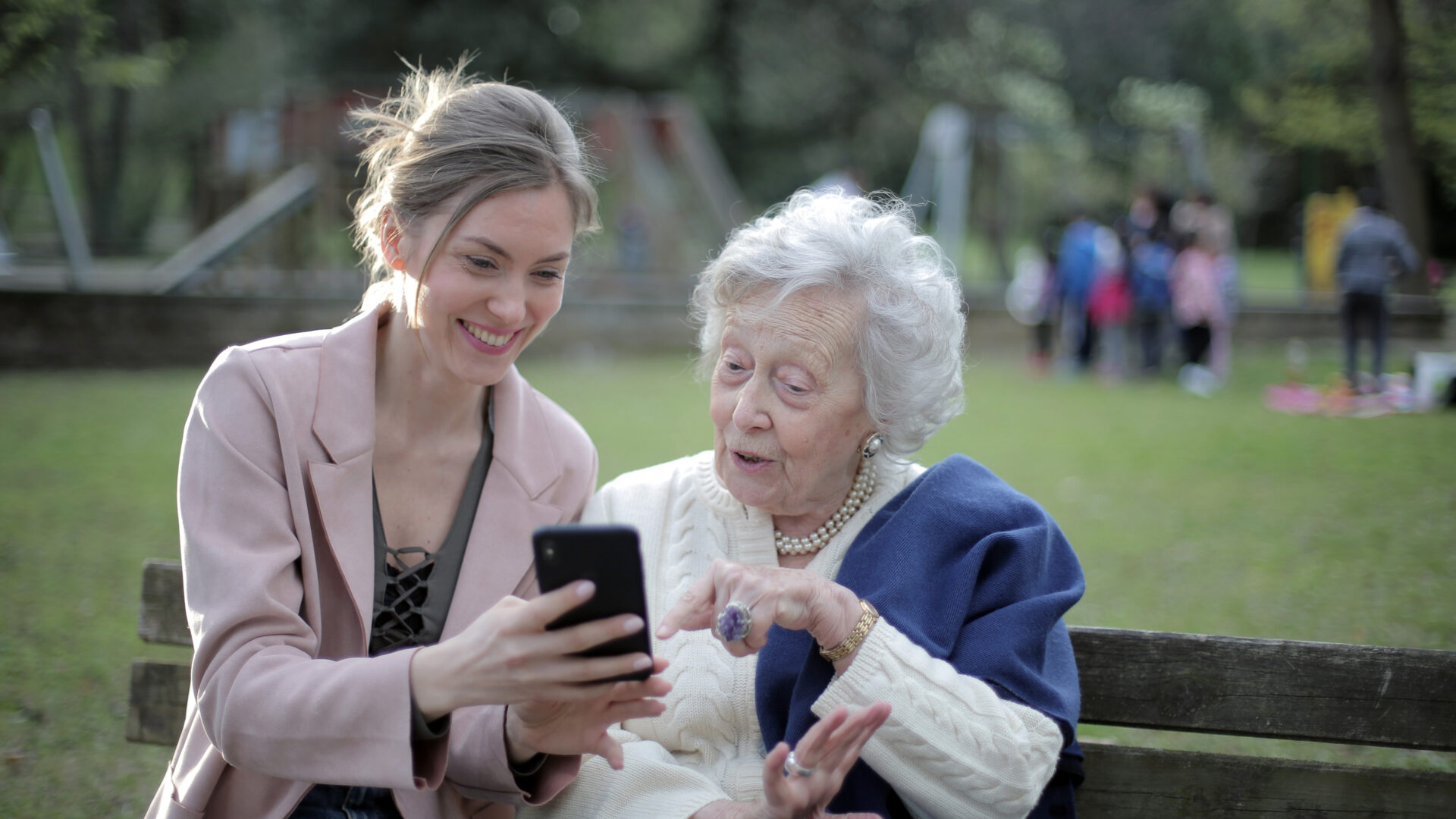 Decoratieve foto van een bejaarde vrouw en een vrouw van middelbare leeftijd die samen op een bankje naar een telefoon kijken