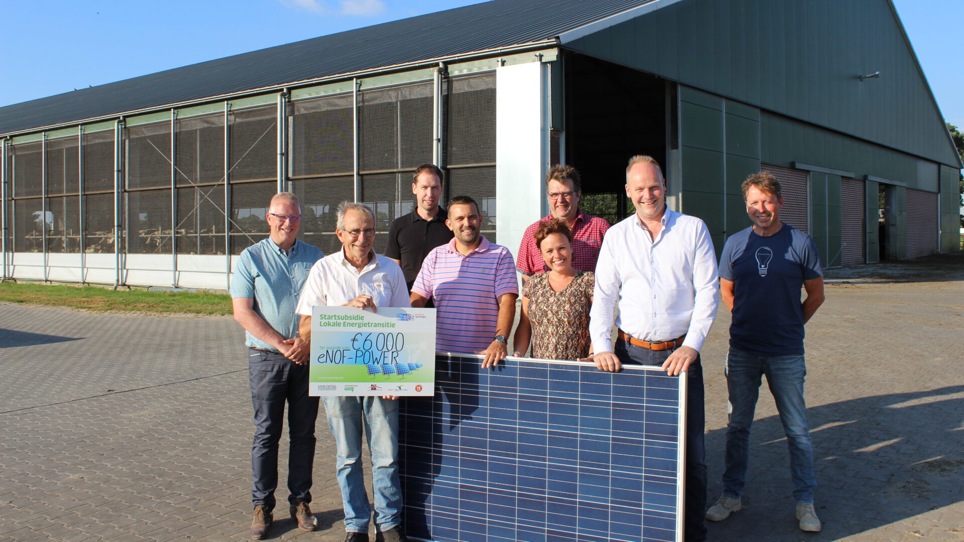 Decoratieve afbeelding van initiatiefnemers van een energiecollectief bij een zonnepaneel en een cheque