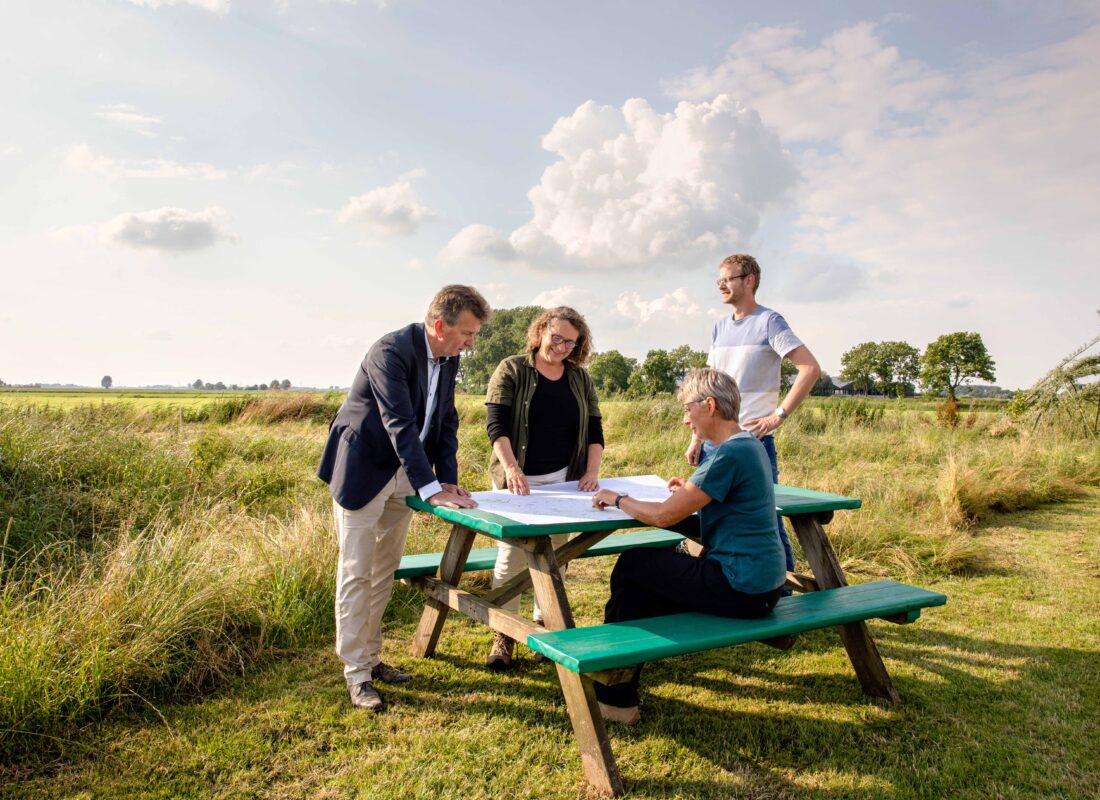 Decoratieve afbeelding van initiatiefnemers van De Landschapswerkplaats om een picknicktafel, pratend over plannen