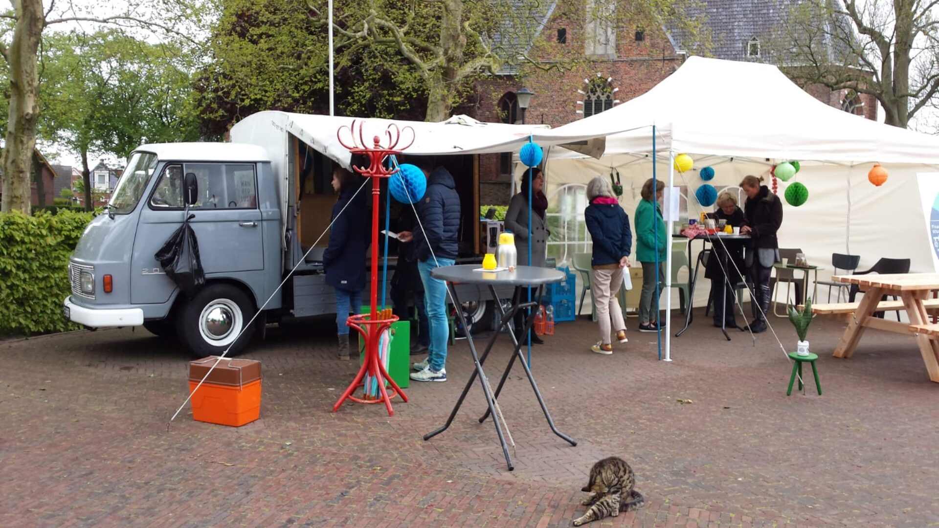 Foto van een busje en een markt waar mensen lopen om ideeën op te halen in Loppersum