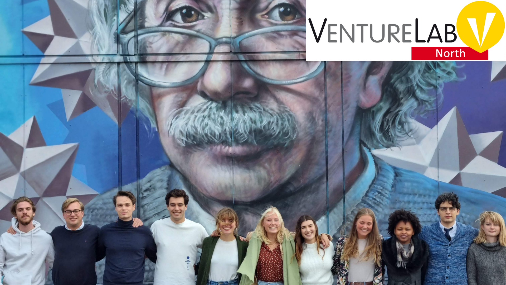 Groepsfoto van de betrokkenen bij VentureLab Noort voor hun gebouw orth met de afbeelding van Albert Einstein