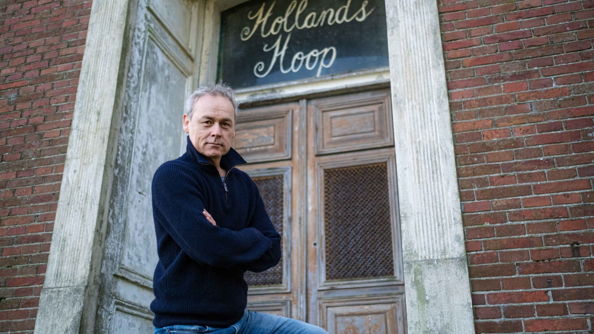 Acteur Marcel Hensema staat voor de boerderij waar de tekst "Hollands Hoop"boven een deur staat uitgebeeld