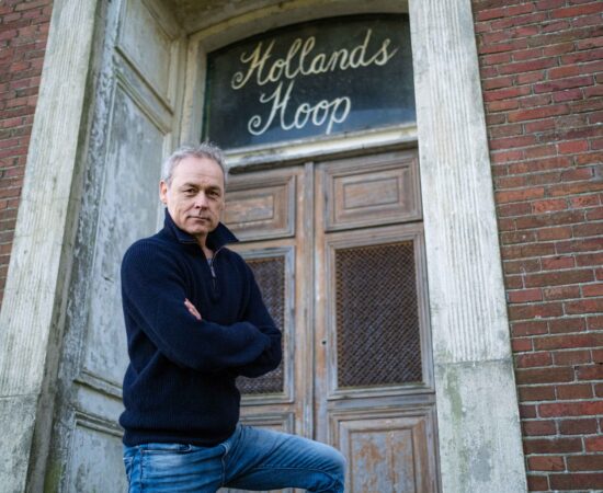 Acteur Marcel Hensema staat voor de boerderij waar de tekst "Hollands Hoop"boven een deur staat uitgebeeld