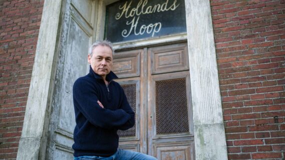 Acteur Marcel Hensema staat voor de boerderij waar de tekst "Hollands Hoop"boven een deur staat uitgebeeld