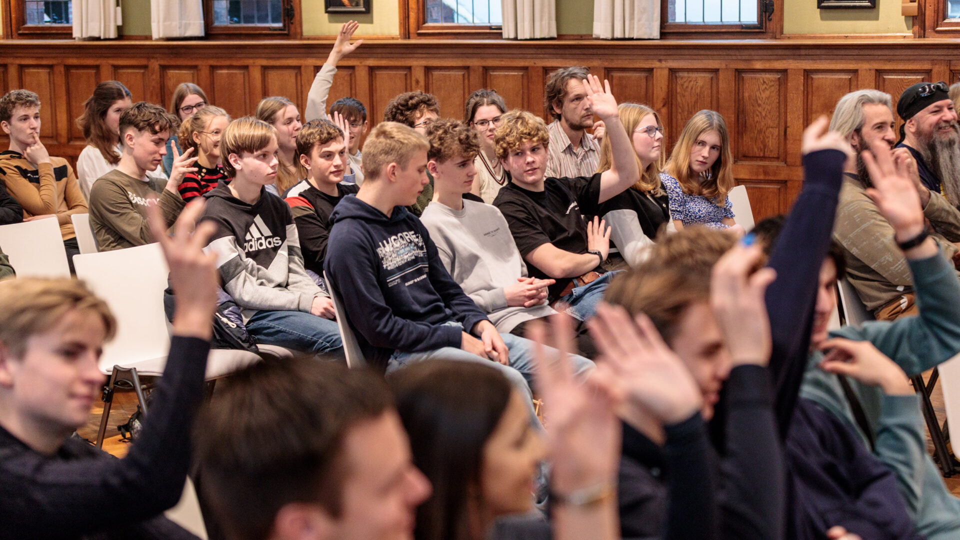 Leerlingen in het publiek steken hand op tijdens de finale van de Scholenchallenge 2023.