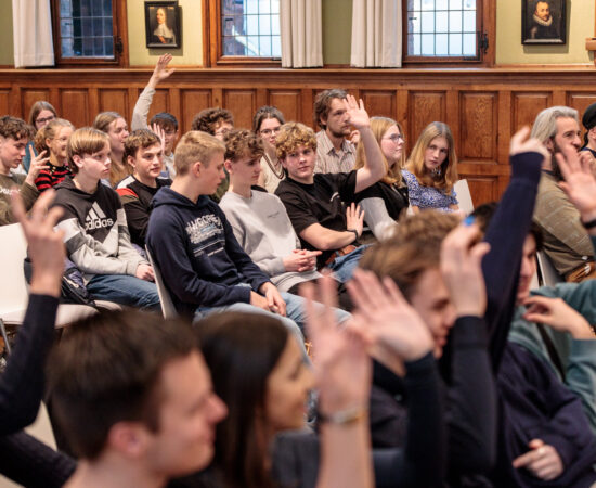 Leerlingen in het publiek steken hand op tijdens de finale van de Scholenchallenge 2023.